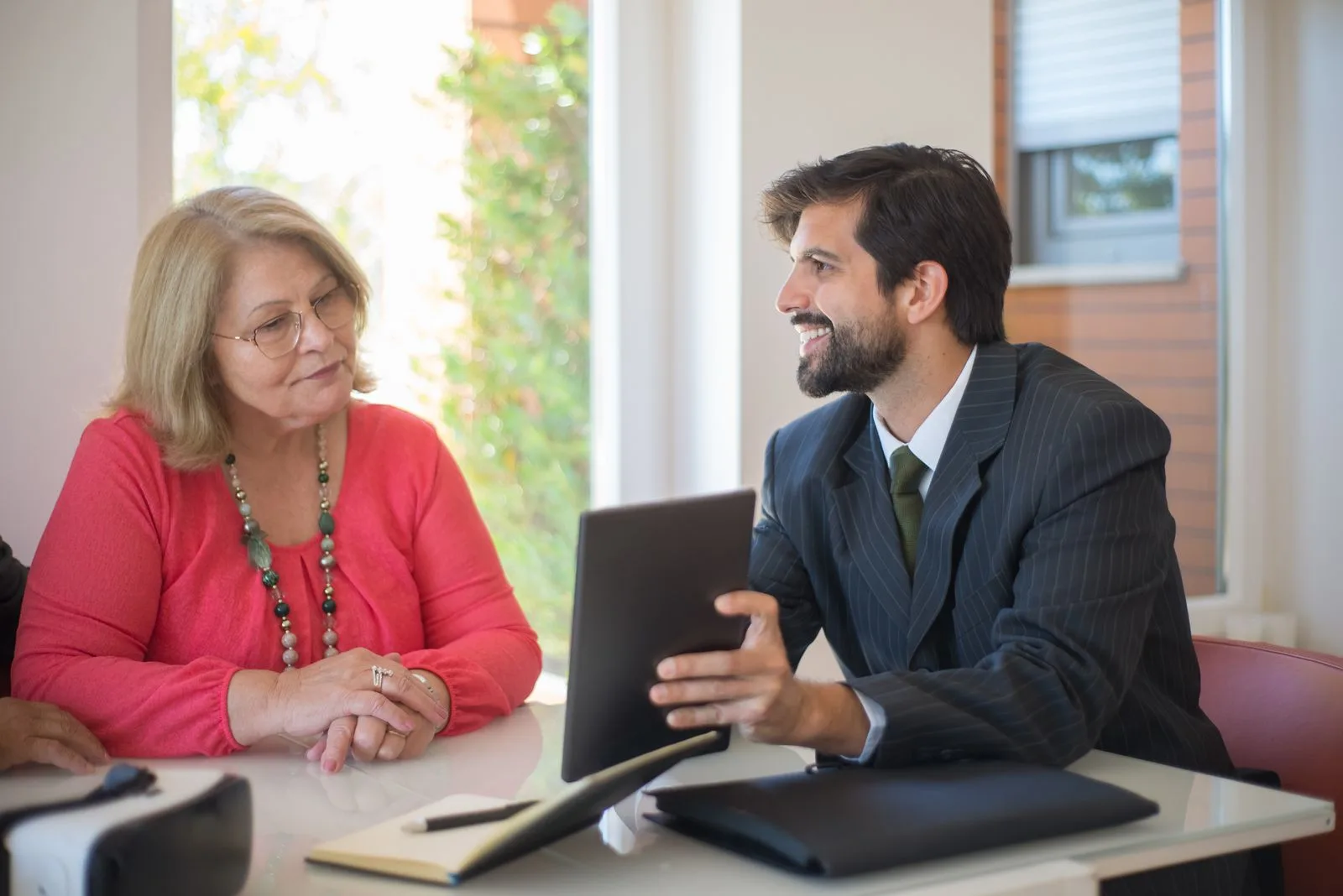 Male business advisor showing tablet content to an older woman client at a bright office table
