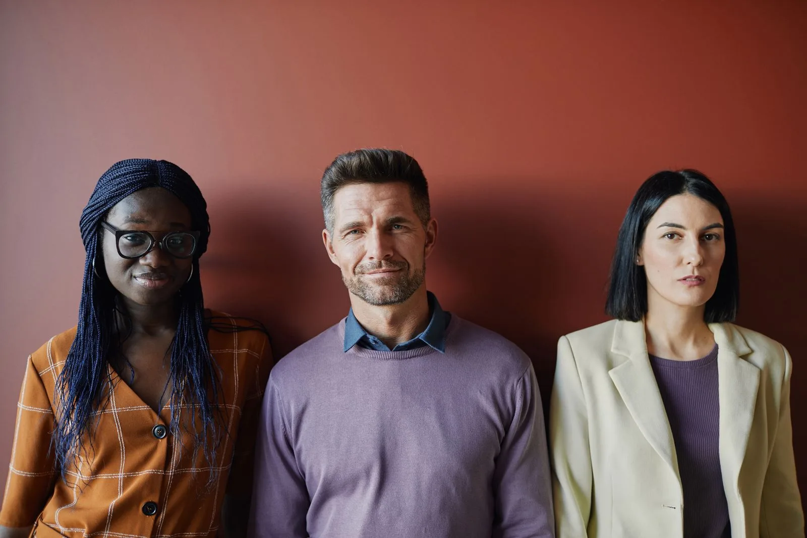 Portrait of three professionally dressed people from different backgrounds standing against a warm terracotta wall