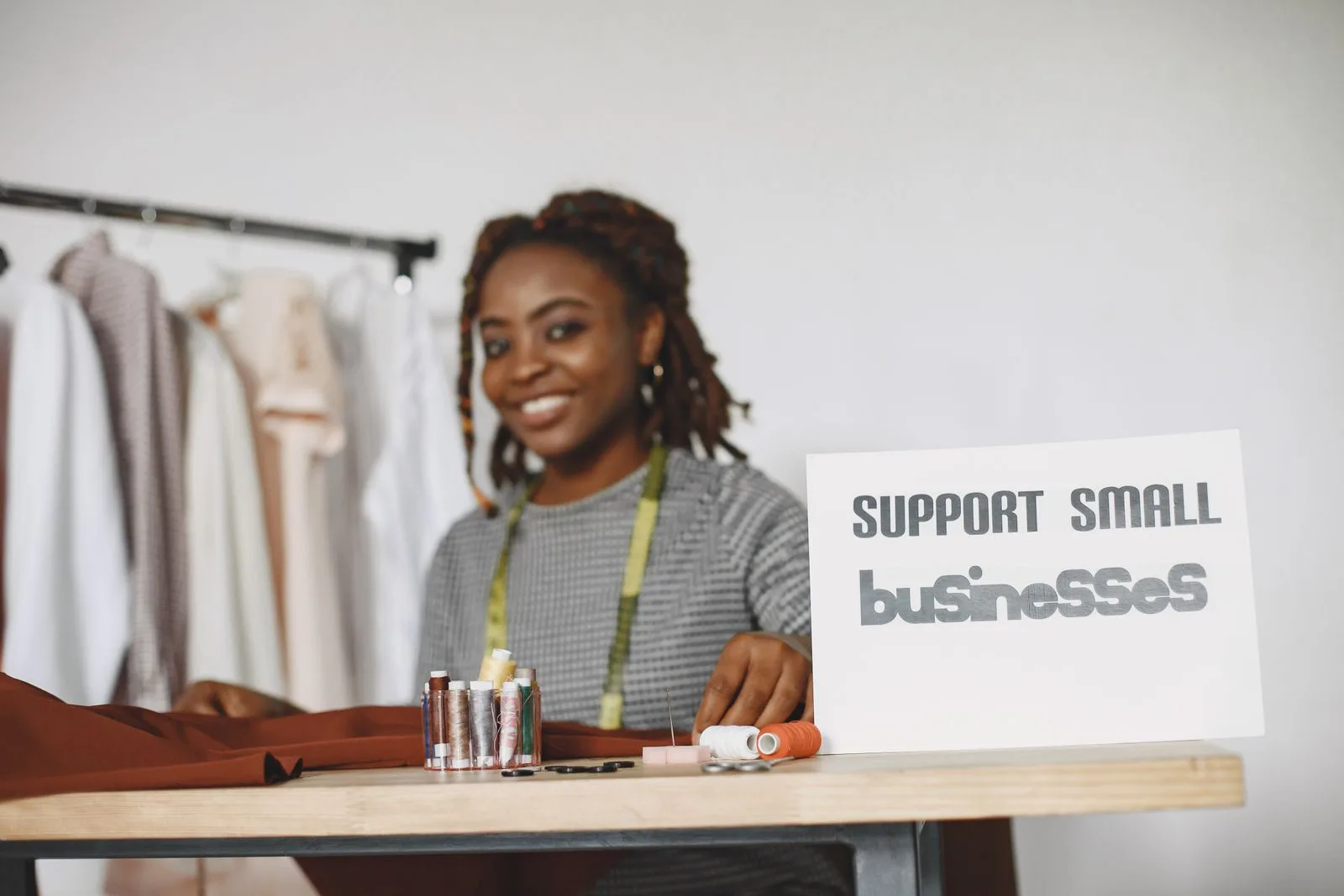 Small business owner in a fashion studio at her worktable next to a Support Small Businesses sign and colorful thread spools