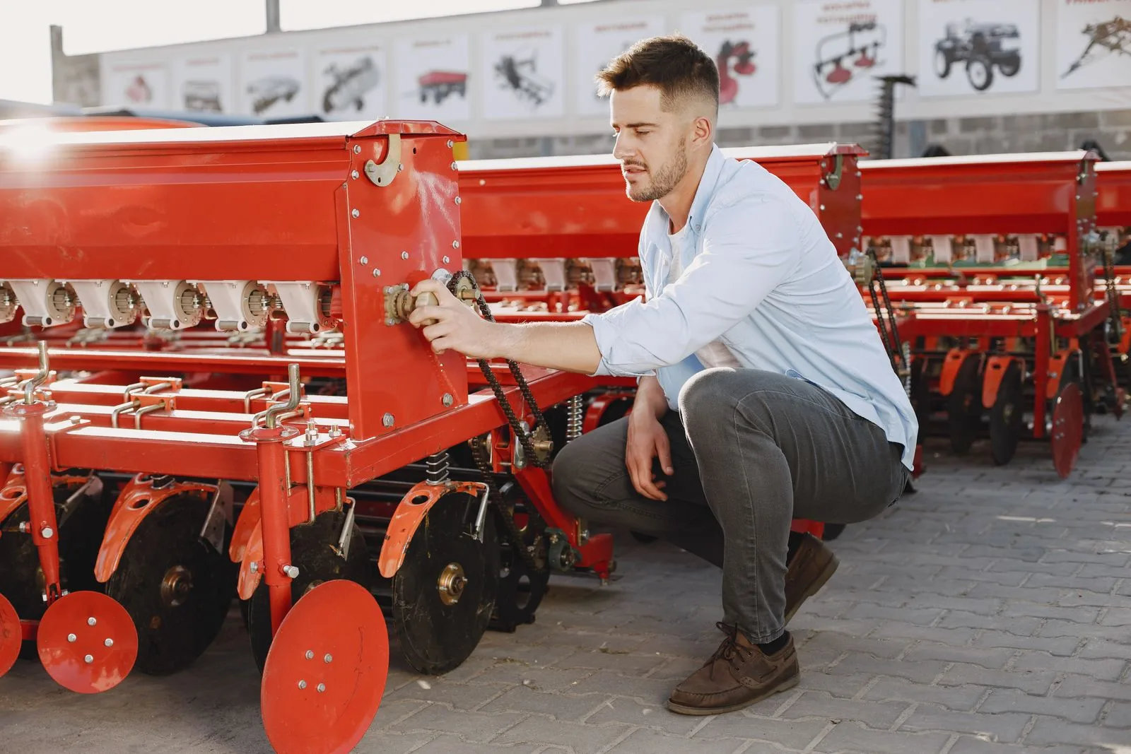 Business owner in a light blue shirt inspecting a large red agricultural planter machine outside a dealer showroom