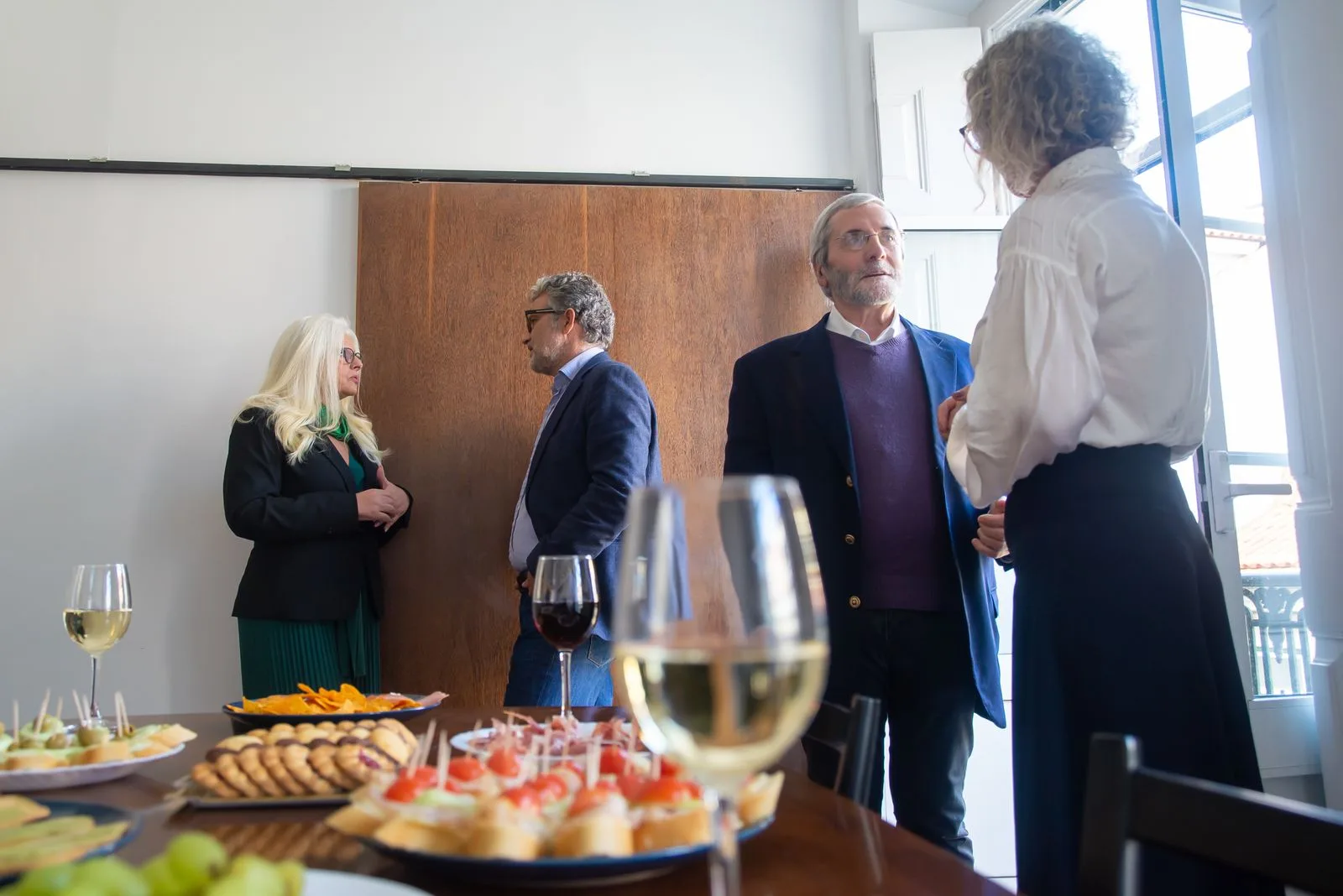 Group of four business professionals talking around a table of appetizers and glasses at a networking reception