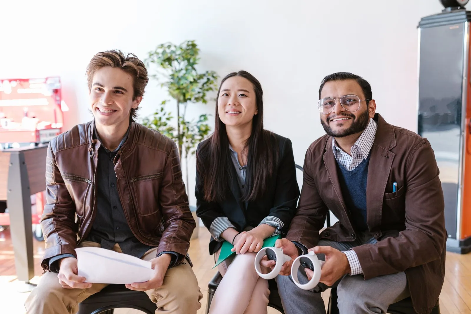 Three smiling startup founders sitting together with product prototypes in a bright office
