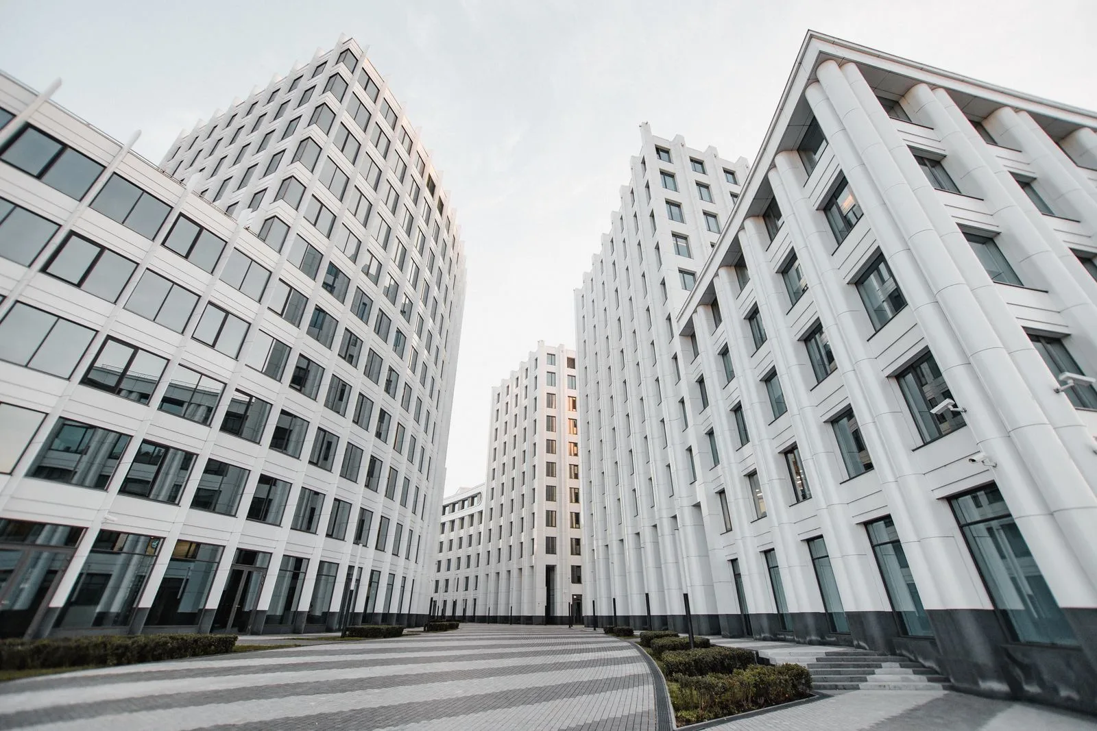 Modern white multi-story commercial buildings with fluted facades along a paved plaza