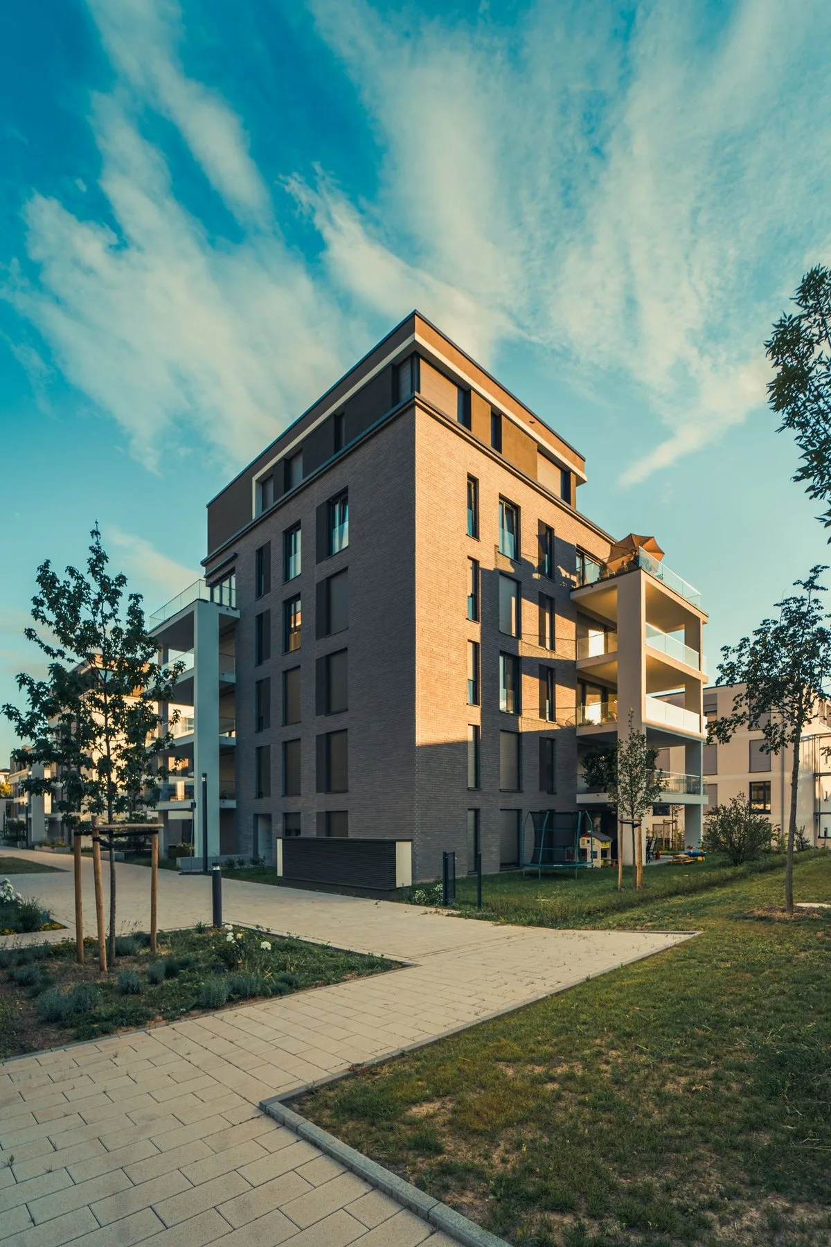 Modern mid-rise brick and glass apartment building beside a green lawn at golden hour