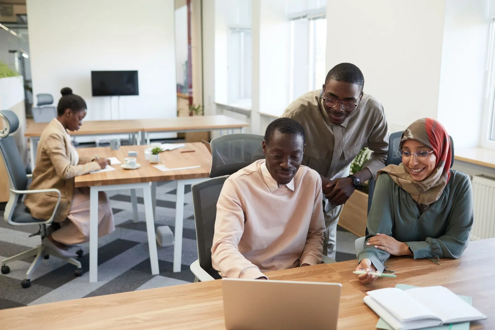 Diverse business team of three collaborating around a laptop in a bright modern office